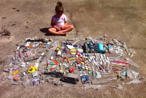 Child sitting with trash collected on a beach.