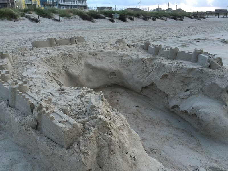A large and deep hole that is part of a sand castle on the beach.
