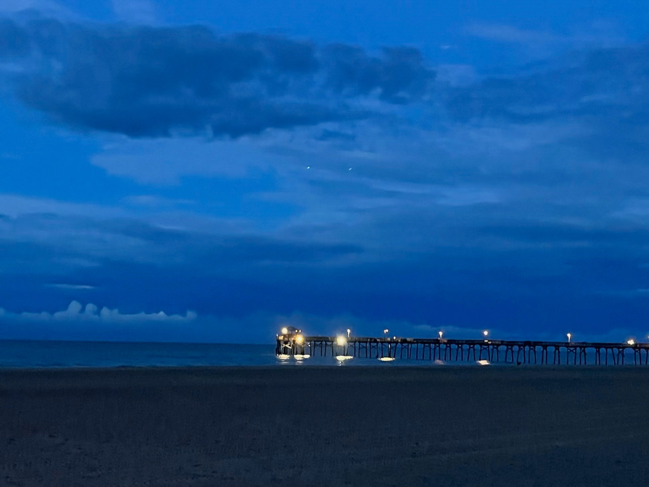 Bright lights on a pier shining toward the beach.