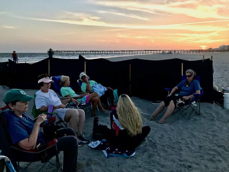 Volunteers sit at sunset at a sea turtle nest that is surrounded by shade cloth to protect the hatchlings from light pollution.